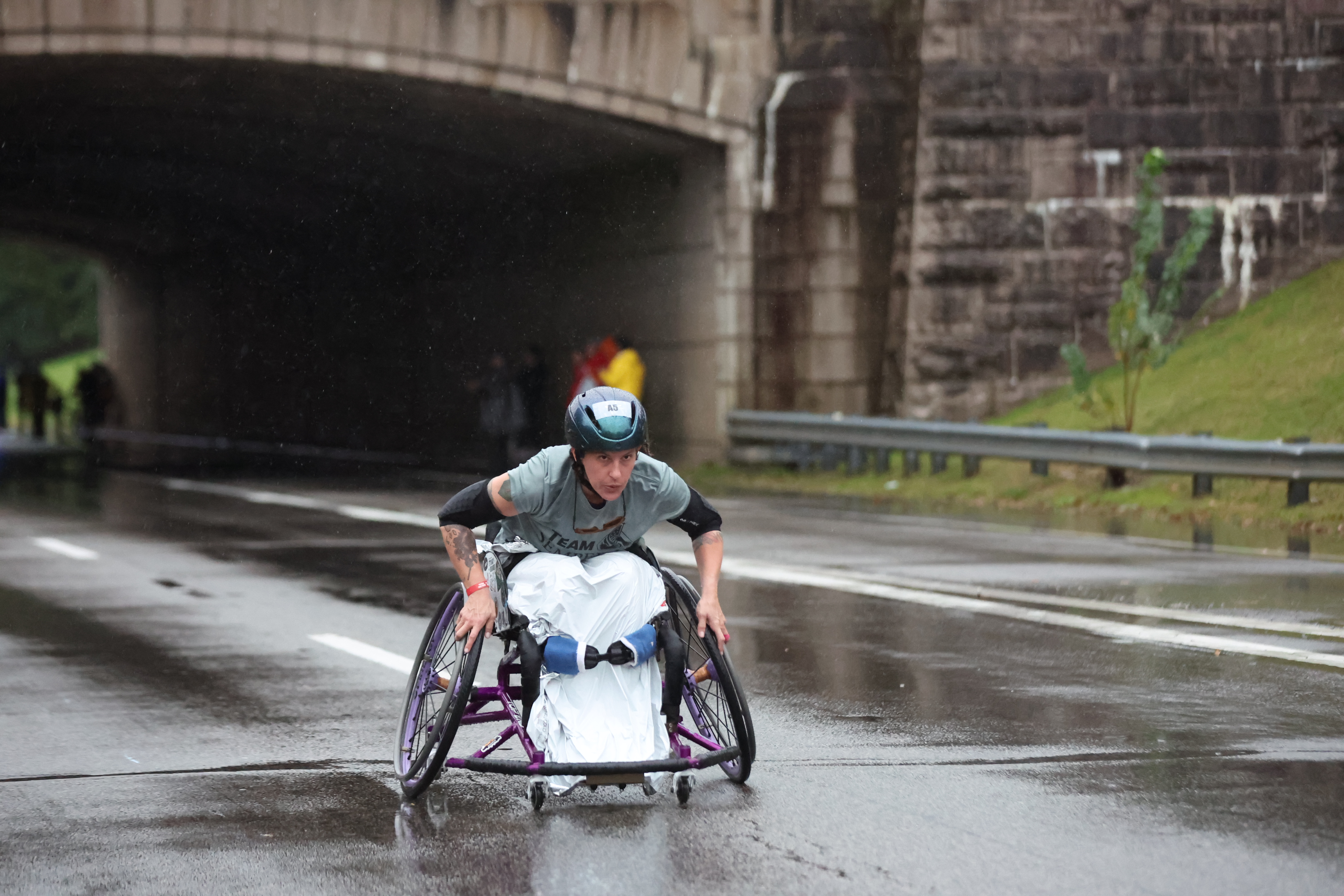 A participant in a racing wheelchair moves along the wet course near mile 1 of the Army Ten-Miler on October 11, 2026.