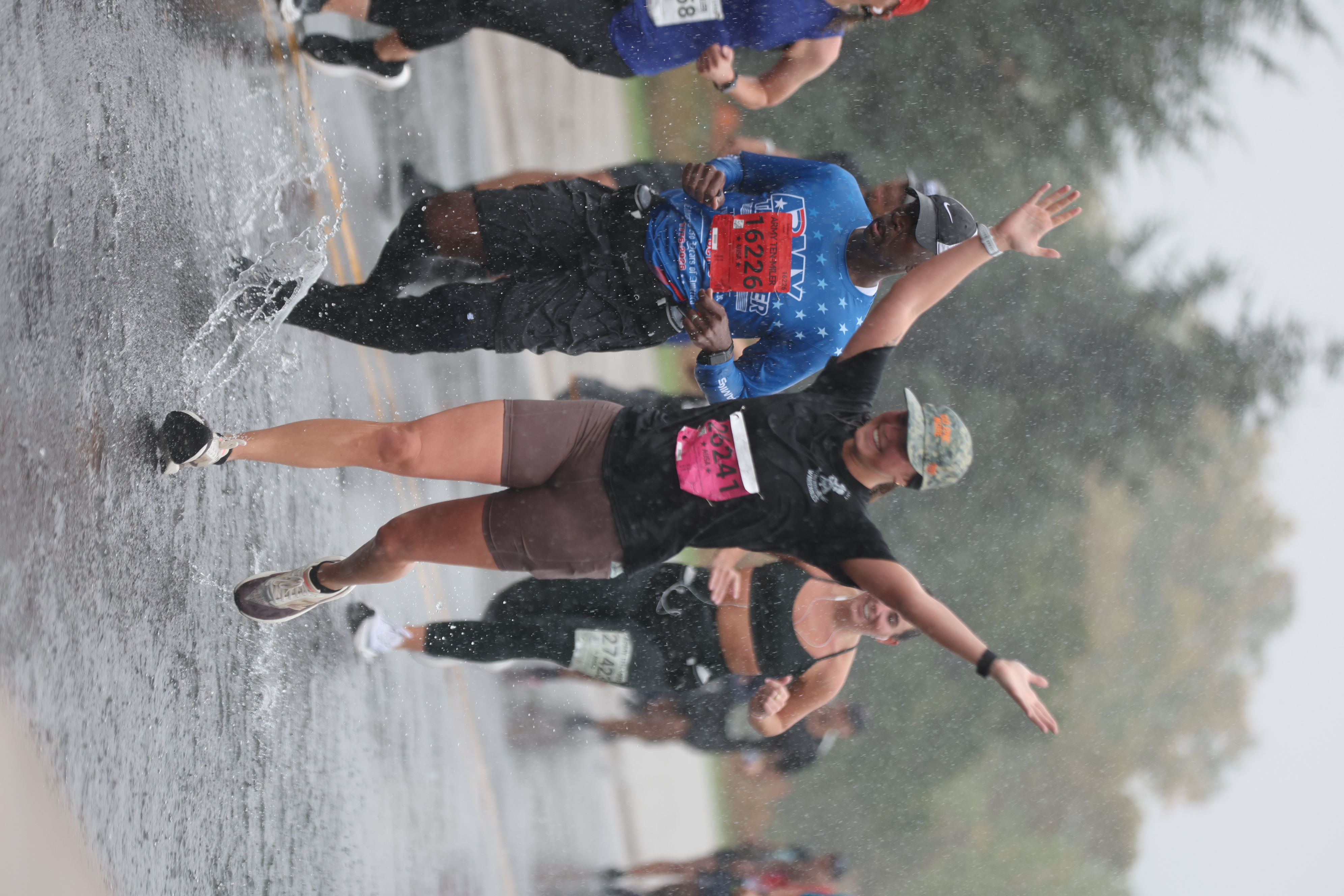A runner raises both arms while splashing through standing water near mile 9.5 of the 42nd annual Army Ten-Miler on October 11, 2026.