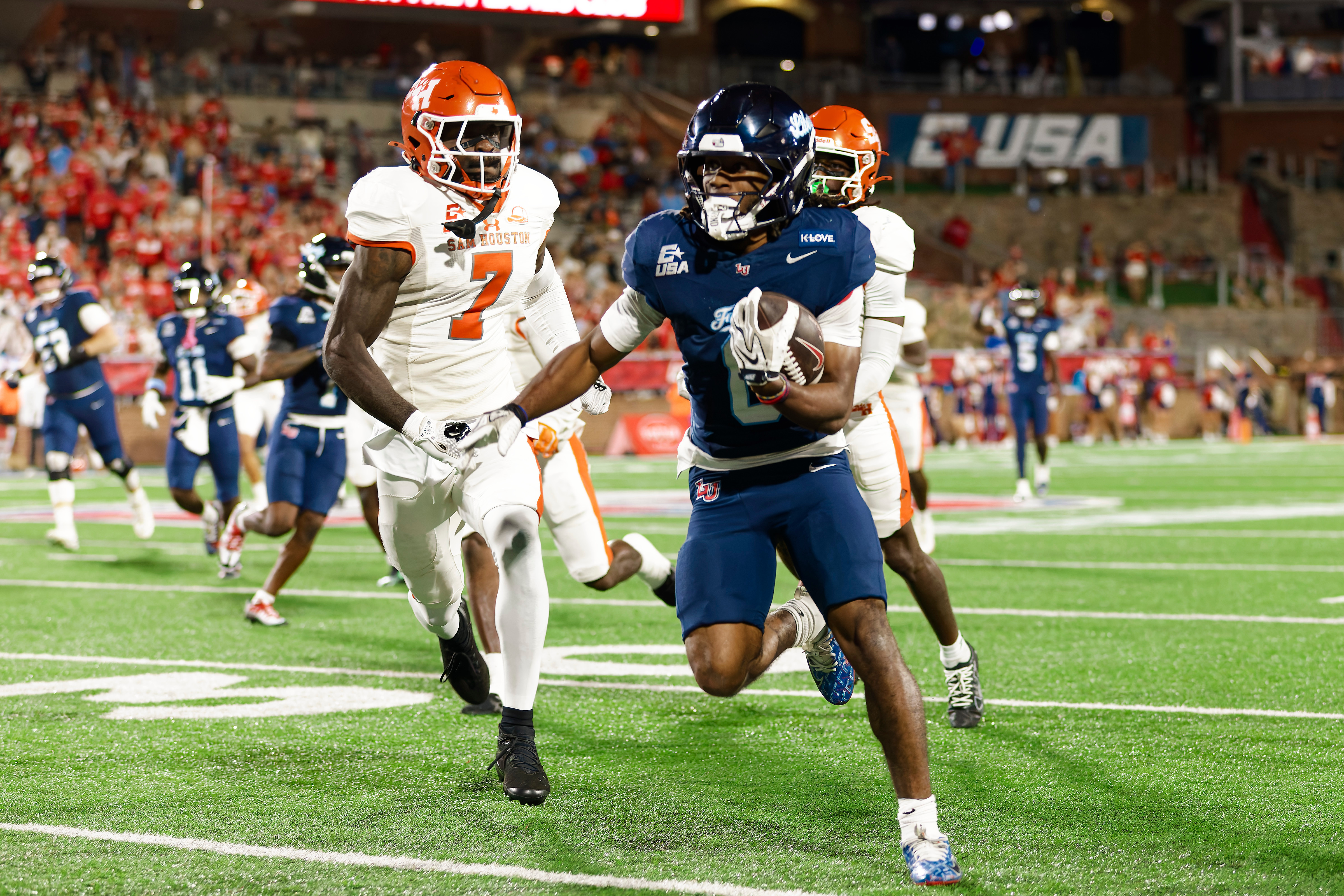 Liberty ballcarrier running alongside Sam Houston defenders
